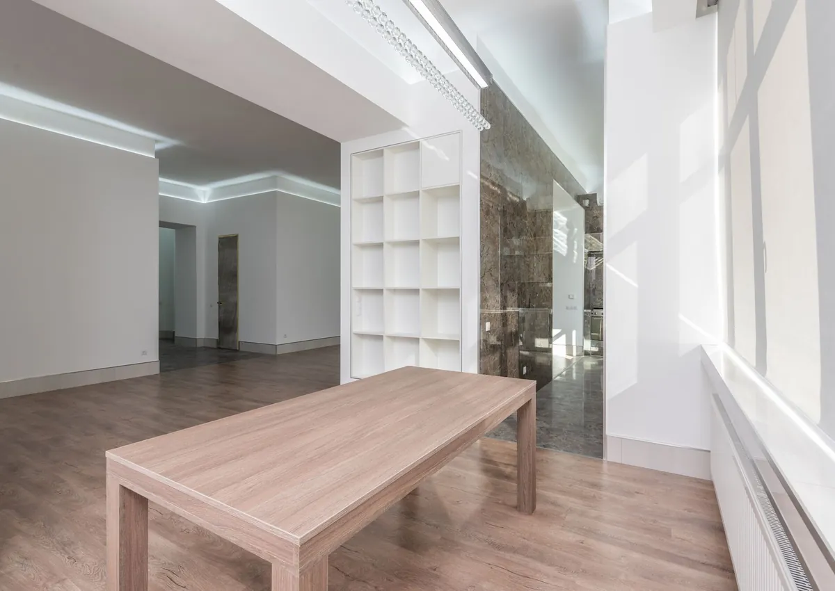 Spacious modern minimalist interior featuring a wooden table, parquet flooring, and natural light.