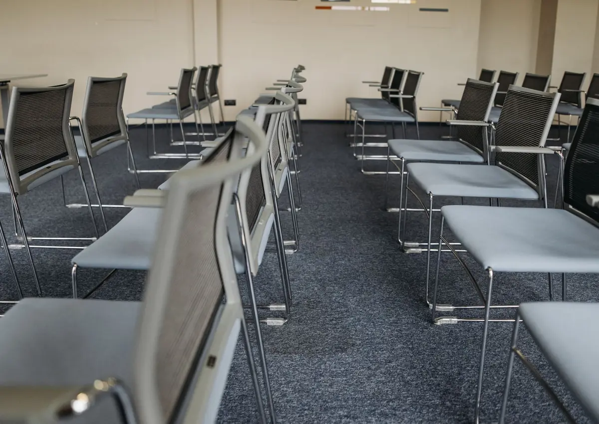 An empty meeting room with rows of modern chairs and carpet flooring, ready for use.