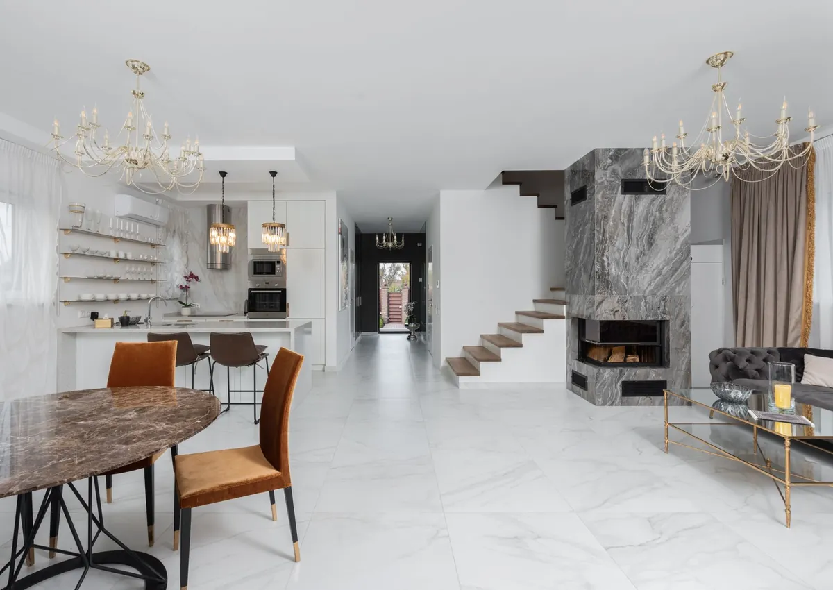 Stylish apartment with chairs at table placed near white kitchen counter in room with couch and side table near fireplace at staircase