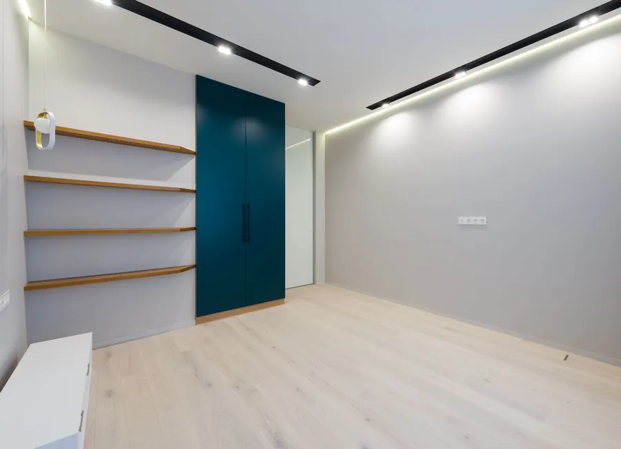 Wooden shelves and wardrobe placed in spacious modern room with laminate floor and bright glowing lamps