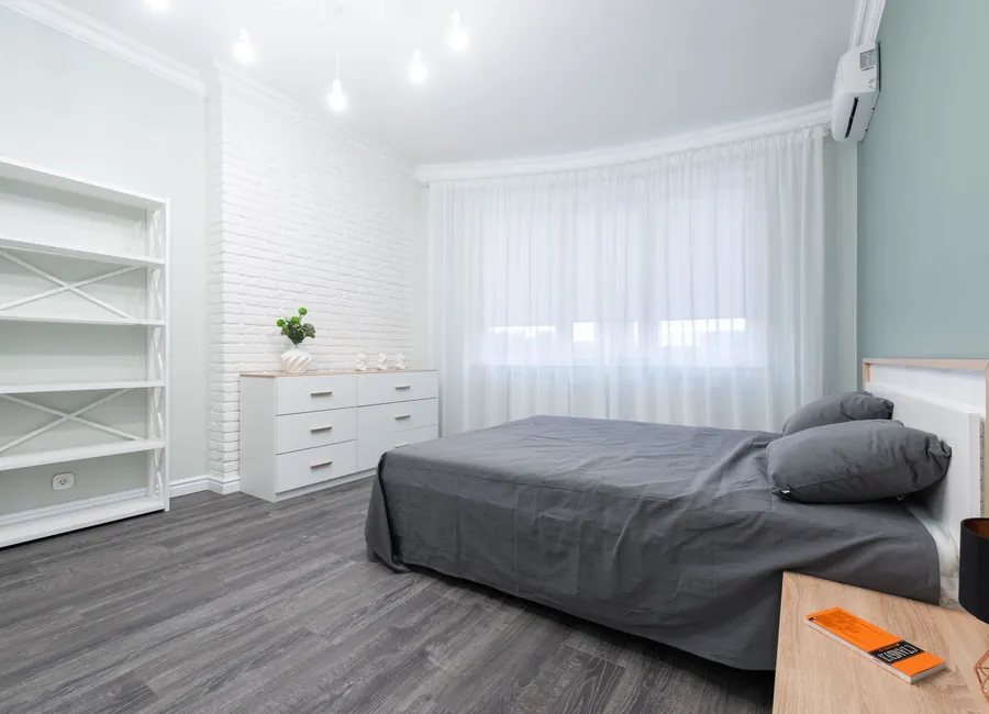 Comfortable bed with soft pillows in cozy bedroom with white walls and furniture and gray laminate floor