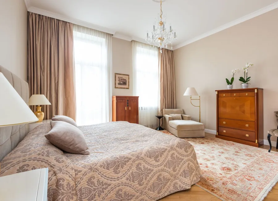 Interior of bedroom with comfortable bed with soft headboard placed near carpet and wooden vintage furniture under chandelier