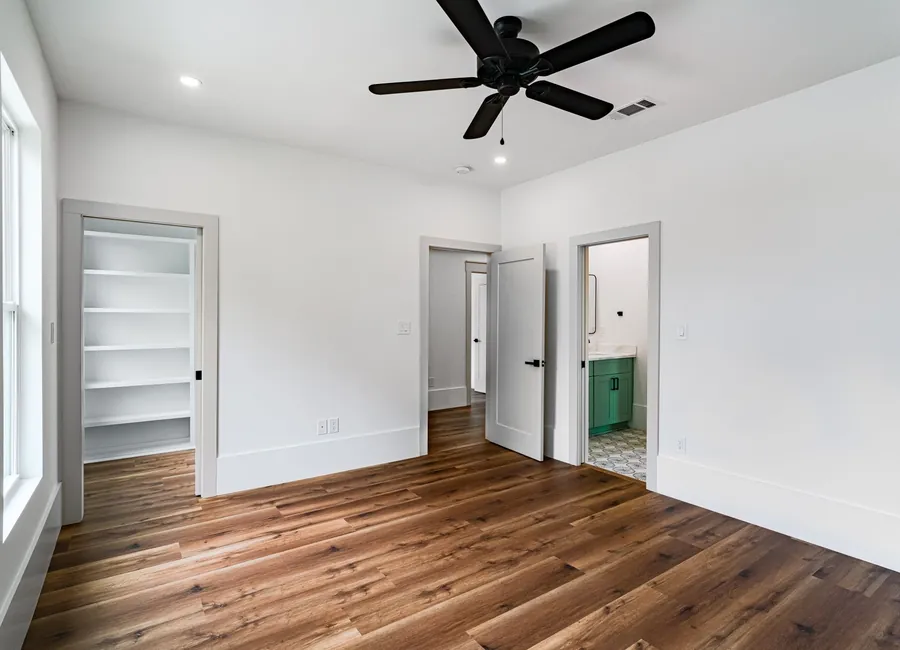 Spacious, minimalistic room with wooden flooring and ceiling fan, ideal for home staging.