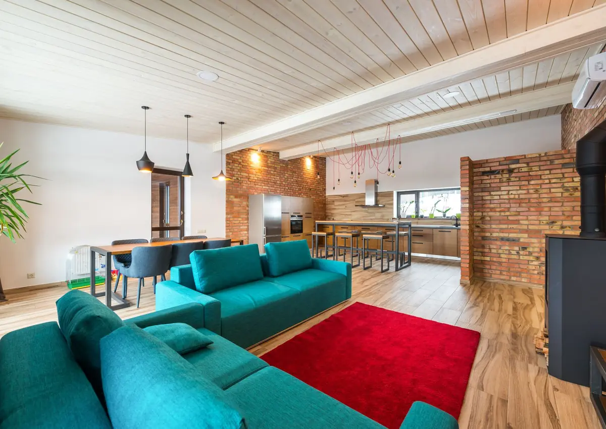 Spacious modern living room featuring brick walls, teal sofa, and red rug.