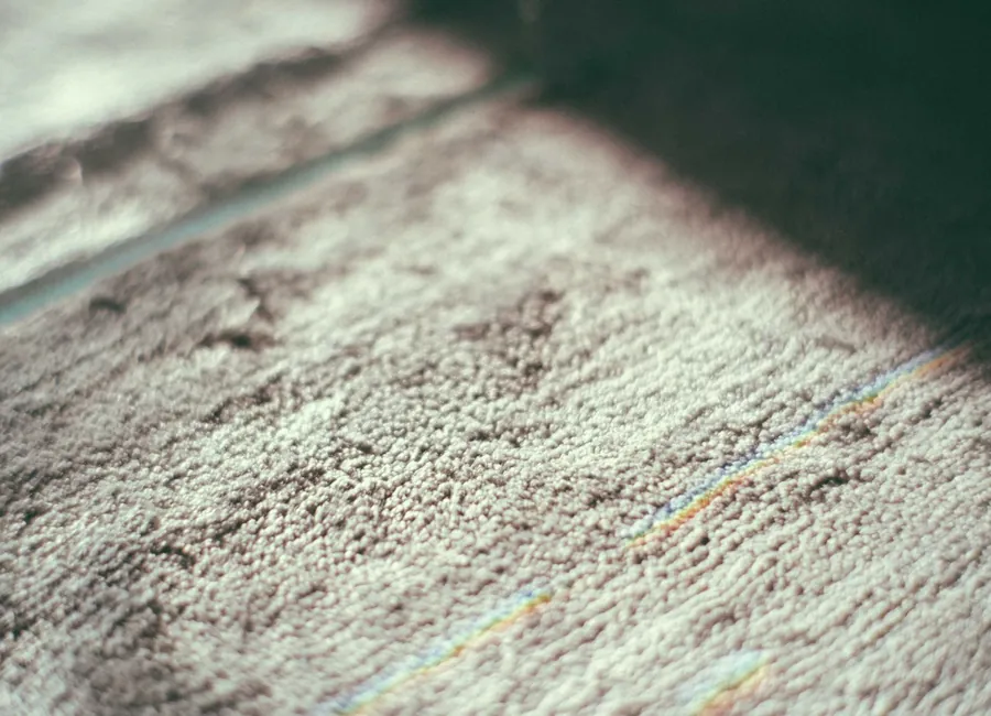Closeup of gray textured carpet with thin colorful lines placed on floor in room with bright sunlight and shadow at home