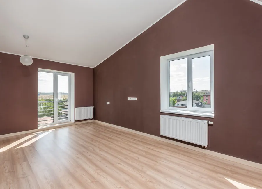 Bright and spacious beige room with brown walls, large windows, and a wooden floor.